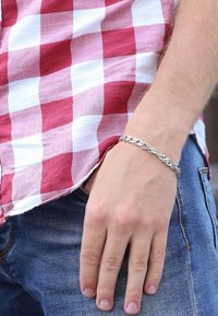 Silver chain bracelet with interlocking links, worn on a hand, with red and white checkered shirt partially visible in the background.