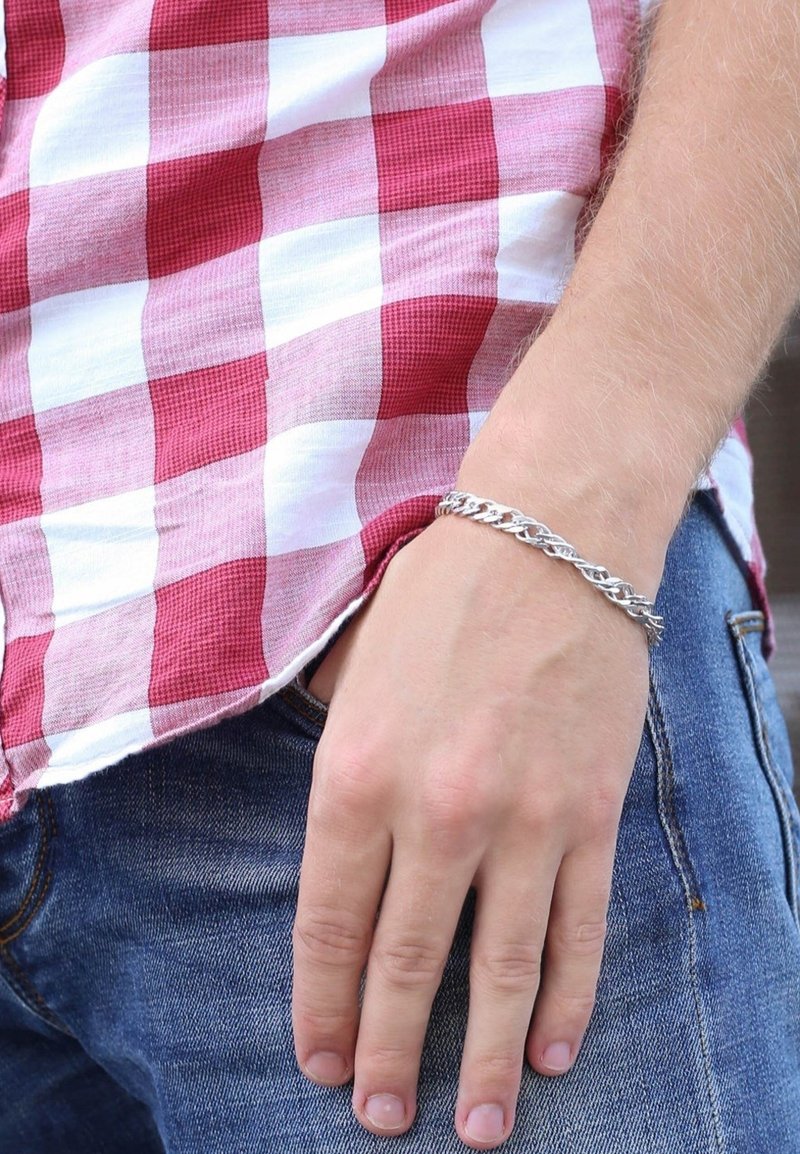 Silver chain bracelet with interlocking links, worn on a hand, with red and white checkered shirt partially visible in the background.