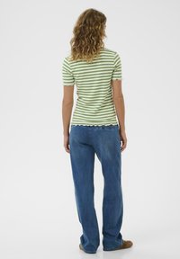 Grün-weiß gestreiftes Kurzarmoberteil mit gewellten Kanten, kombiniert mit locker sitzenden blauen Jeans.