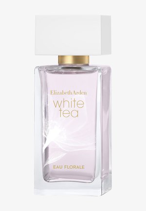 Flacon de parfum en verre transparent contenant un liquide rose pâle, décoré d'un motif floral blanc, texte doré « Elizabeth Arden white tea eau florale » et bouchon rectangulaire blanc.