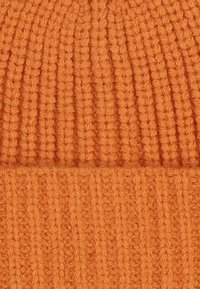 Knitted beanie in vibrant orange. Features a ribbed texture with vertical lines, soft fabric, and a folded edge at the bottom.