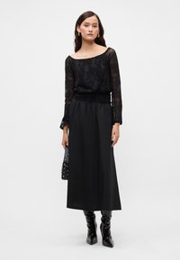 Μαύρη δαντελένια μπλούζα μακρύ μανίκι με λουλουδάτο σχέδιο, συνδυασμένη με ψηλόμεση μαύρη φούστα και γυαλιστερές μαύρες μπότες έως το γόνατο. Μαύρη τσάντα με στρας.