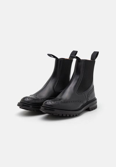Botine Chelsea din piele neagră cu panouri elastice pe laterale, detalii brogue pe vârf și o talpă din cauciuc rezistentă pentru aderență.