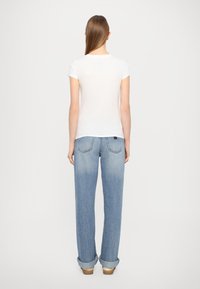 T-shirt bianco a maniche corte e jeans a gamba larga blu chiaro con orli arrotolati. I jeans presentano un design discreto delle tasche posteriori e una minima presenza di marchio.