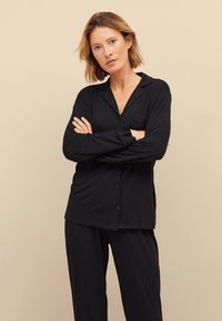 Zwart pyjama set bestaande uit een knoopsluiting lange mouwen top met een zak en bijpassende broek. Gladde stof met een comfortabele pasvorm en kraagontwerp.