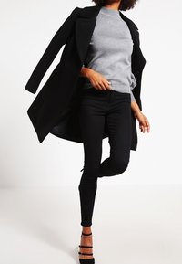 Black long coat with lapel, gray ribbed turtleneck sweater, black skinny jeans, and black strappy heels. Smooth textures and fitted silhouette.