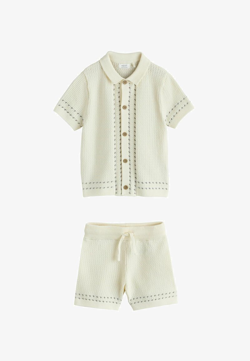 Krémová pletená košeľa s krátkym rukávom na zapínanie na gombíky s golierom a zladené šortky so sťahovacou šnúrkou, oboje s jemnými sivými vzormi švov.