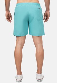 Shorts da bagno turchesi realizzati in tessuto leggero. Vita elasticizzata, tasca sul retro e orli cuciti. Indossati con sneakers bianche.