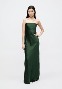 Rochie de seară verde închis, fără bretele, realizată dintr-un material satinat neted, cu o croială lungă până în podea, care cade elegant.