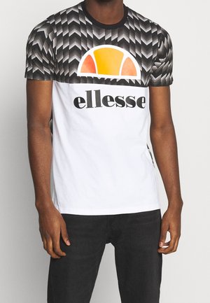 Mężczyzna ubrany w t-shirt Ellesse z krótkim rękawem, z czarno-szarym wzorem w jodełkę na górze i białą dolną częścią.
