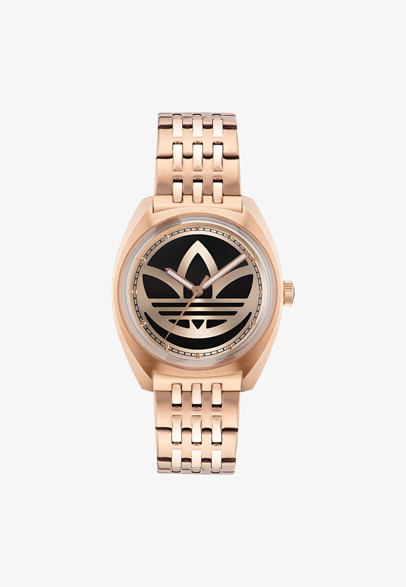 Rožu zelta pulkstenis ar melnu ciparnīcu, kas izceļas ar lielu logo dizainu. Tam ir saistīts metāla aproce un ģeometriska formas korpuss. Apaļa stikla virsma.