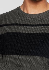 Strickpullover mit horizontalen Streifen in Dunkelgrau, Schwarz und Hellgrau. Strukturiertes Material mit Rundhalsausschnitt und gerippten Bündchen.