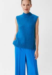 Strickoberteil ohne Ärmel in hellblau mit hohem Kragen, das eine strukturierte Oberfläche und einen gerippten Saum aufweist, kombiniert mit einer passenden hellblauen weiten Hose.