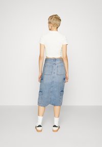 Fustă midi din denim de culoare albastru deschis, cu buzunare tip cargo, o formă ușor ajustată și tiv brut. Asortată cu șosete albe și adidași.