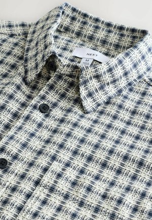 Checkered button-up shirt in navy and cream. Soft fabric with a textured pattern, featuring a standard collar and black buttons.