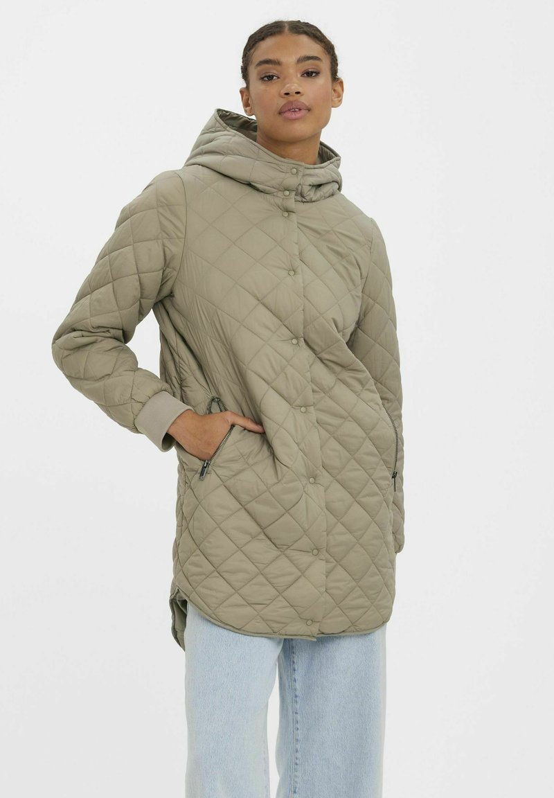 Manteau long matelassé en beige clair avec capuche, doté d'une fermeture à pression et de poches latérales, fabriqué à partir d'un tissu lisse et léger.