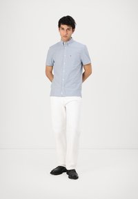 Short-sleeve, light blue striped shirt with button-down collar and logo detail, paired with white pants and black shoes.