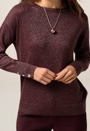Bordeauxrode trui met metallic glinstering, ronde hals, lange mouwen en decoratieve knopen bij de manchetten. Getailleerde gebreide structuur.