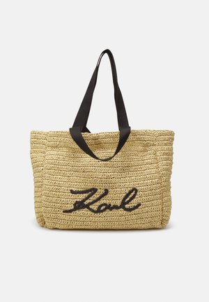 Woven beige tote bag with black fabric handles and black script "Karl" embroidered on the front.
