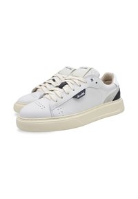White leather sneakers with cream rubber sole, lace-up design, perforated detailing, and black accent on the side featuring a logo.
