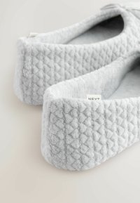 Papuci de casă gri din pluș cu un model texturat matlasat, margini rotunjite și interior moale. Etichetă vizibilă pe lateral.