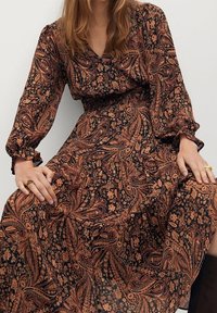 Robe à manches longues noire avec des motifs floraux et paisley orange complexes. Présente une taille cintrée et une jupe fluide. Texture de tissu douce.