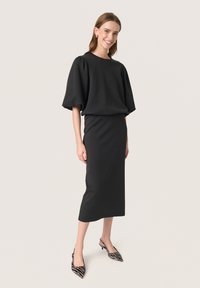 Czarna sukienka o luźnym kroju, z bufiastymi rękawami i długości do kolan, zestawiona z butami na obcasie typu slingback zakończonymi w szpic, w wzór zebry.