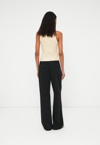 Béžový top na ramínka a černé široké kalhoty. Top má přiléhavý střih a kalhoty mají hladkou strukturu s kapsami.