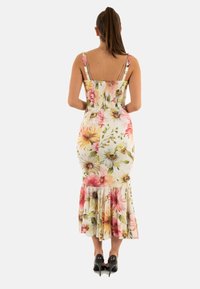 Abito midi floreale con spalline sottili, caratterizzato da un corpino aderente, una schiena arricciata e un orlo a volant. I colori includono rosa, giallo e verde.