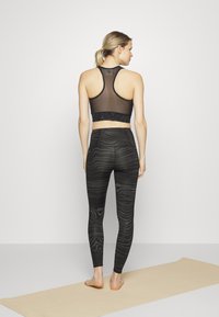 Top desportivo preto com um painel transparente e acabamento decorativo em renda, combinado com leggings pretas texturizadas apresentando um padrão ondulado.