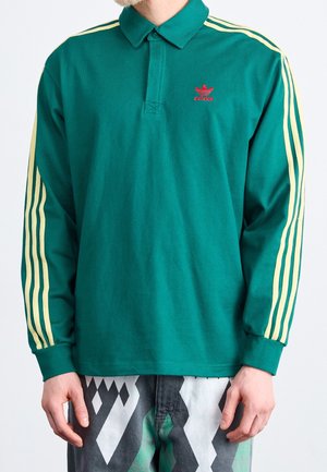 Zielona polo z długim rękawem i kołnierzykiem, z żółtymi trzema paskami na rękawach oraz małym czerwonym logo na piersi.