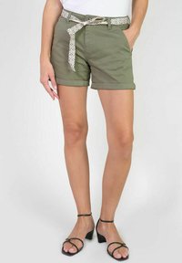 Shorts en coton vert olive avec des ourlets retroussés, dotés d'une ceinture à motifs blancs, de poches avant et d'une coupe ajustée. Associés à des talons noirs à brides.
