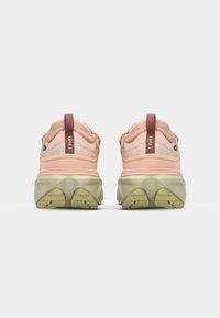 Des chaussures de randonnée roses dotées d'une tige en maille et synthétique, d'une semelle rembourrée et d'une semelle extérieure texturée verte, contrastées par un tirant brun.