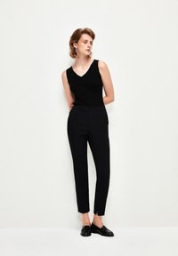 Svart ärmlös topp med V-hals, parat med slim-fit svarta byxor med en subtil slits vid vristen, bärs med svarta loafers.