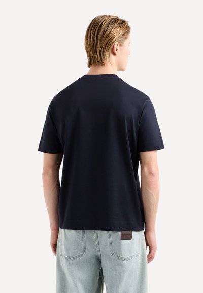 T-shirt en coton bleu marine avec une coupe décontractée, des manches courtes et un détail au niveau du col au dos. Associé à un jean en denim délavé.