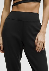 Schwarze Sporthose mit hohem Bund, glattem Material und minimalen Nähdetails, entworfen für Komfort und Flexibilität.