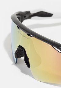 Lunettes de sport noires au design épuré, dotées d'un grand verre dégradé aux teintes jaunes et bleues, et d'accents sur le repose-nez ajustable.