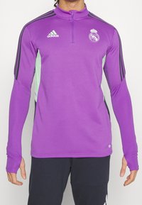 Lila träningströja med långa ärmar och kvartszipskrage, med svarta Adidas-ränder och en ljusgrön detalj på sidorna.