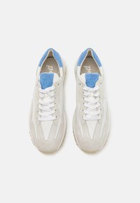 Lys grå sneakers med blå aksenter, laget av en kombinasjon av lær og semsket skinn, med snøring og teksturerte gummisåler.