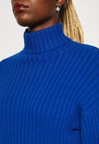 Geribbelde coltrui in levendig blauw. Voorzien van verticale strepen, een hoge kraag en een textuurgebreide stof. Zacht en nauwsluitend ontwerp.