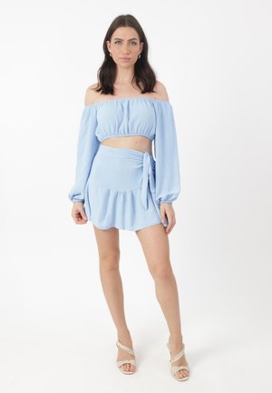 Hellblaues Off-Shoulder-Crop-Top mit langen Ärmeln und einem passenden Wickelrock mit Rüschensaum. Glattes, strukturiertes Material.