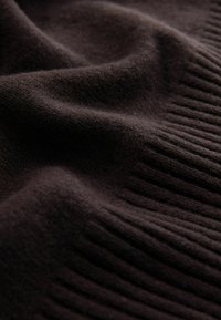 Brauner Strickstoff mit weicher Textur, der eine Kombination aus glatten und gerippten Mustern bietet und Tiefe und Wärme betont.