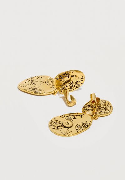 Δύο σκουλαρίκια με κλιπ σε υφή χρυσού τόνου, με ακανόνιστο οβάλ σχήμα και μαύρα στίγματα σε λευκό φόντο.