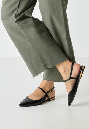 Zwarte leren slingbacks met puntige neus, een dunne enkelband en een kleine hak met gouden accenten, gecombineerd met olijfgroene cropped broek.