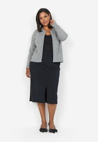 Grå stickad cardigan över en svart topp, kombinerad med en svart pennkjol med en framre slit. Svarta skor med rosettdetaljer.