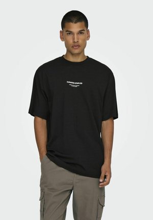 Sort oversized t-shirt i bomuld med korte ærmer. Har hvid trykt tekst "CURATED STAPLES" på brystet. Simpelt og minimalistisk design.
