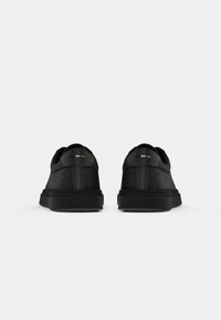 Schwarze Sneakers mit strukturiertem Obermaterial, runder Zehenpartie und niedrigem Profil. Merkmale subtile Akzente in Weiß und Gold auf der Rückseite. Gummisohle.