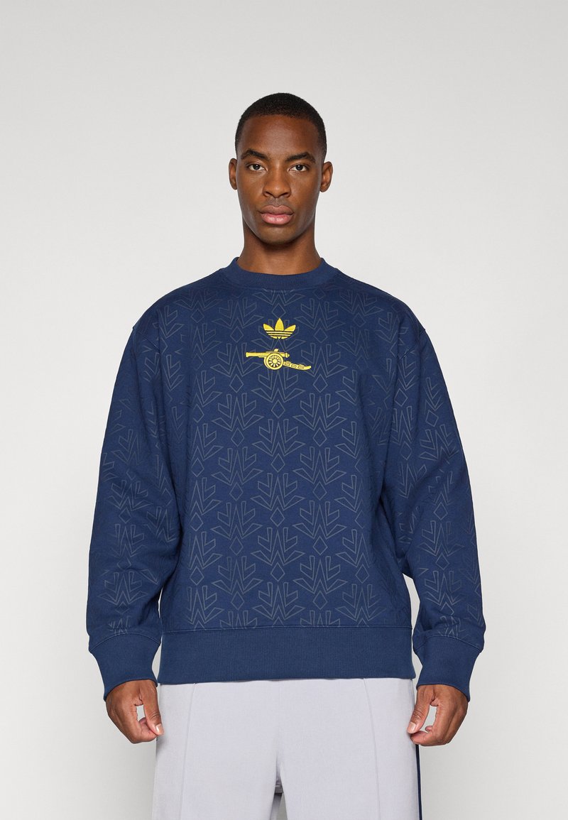Marineblauwe sweatshirt met een gestructureerd bladerenpatroon, voorzien van een gele logo in het midden. Lange mouwen, geribde manchetten en een ronde halslijn.