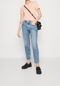 Camiseta de cuello redondo rosa claro, jeans azul de tiro alto con un corte holgado y mocasines negros gruesos. Pequeño bolso negro cruzado.