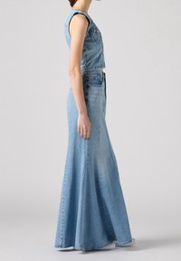 Vestido de mezclilla con parte superior corta sin mangas y falda larga acampanada. Color azul claro con una textura suave y detalles de costura visibles.